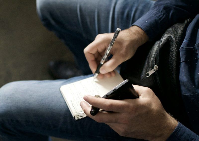 Des mains qui prennent des notes en tenant un téléphone.